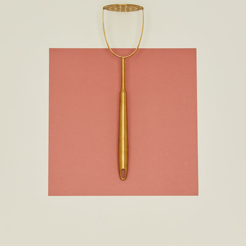Brass potato masher on pink paper