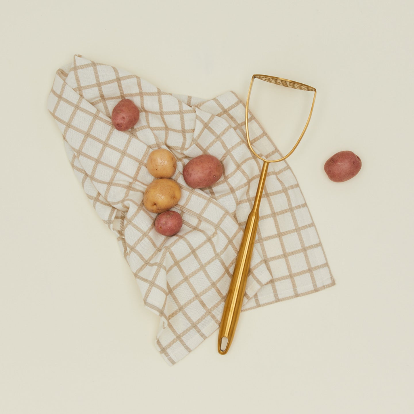 Brass potato masher with a kitchen towel and potatoes