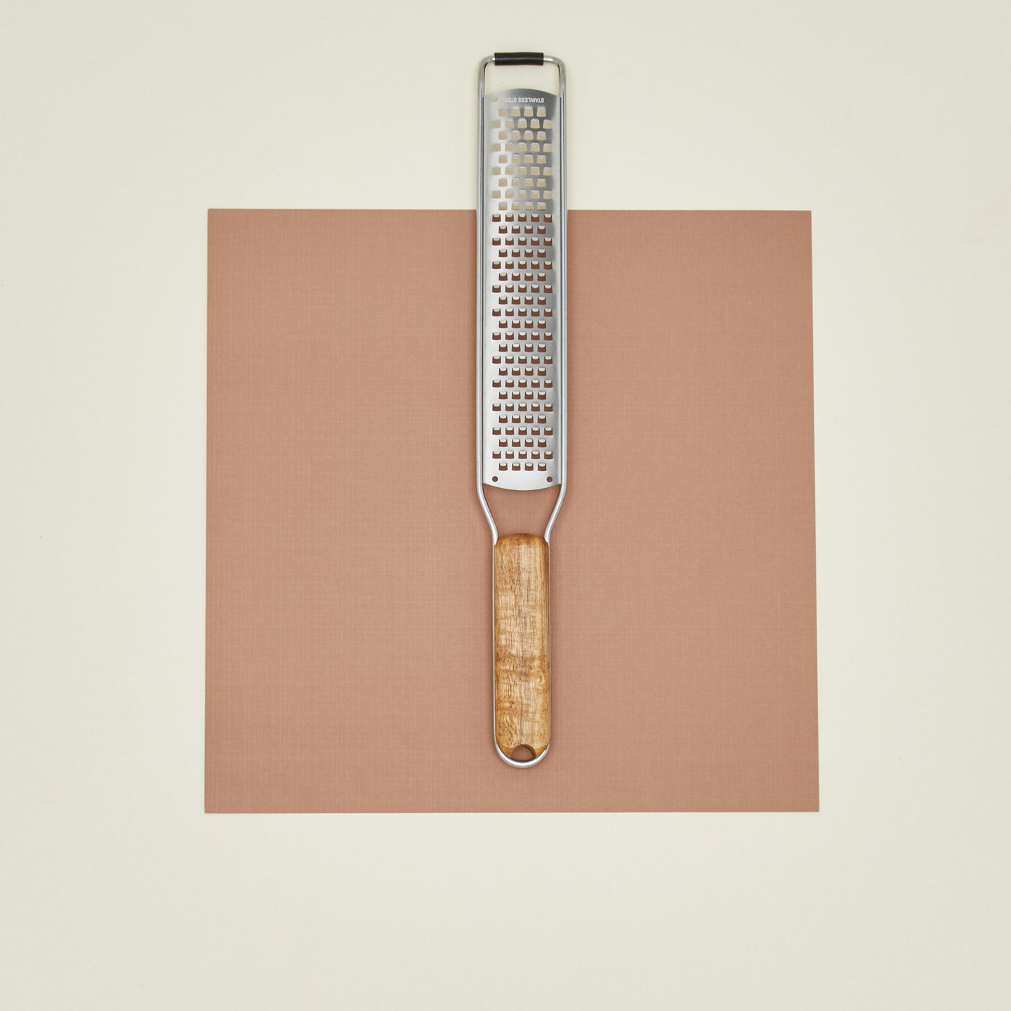 Grater with wooden handle on a brown square background