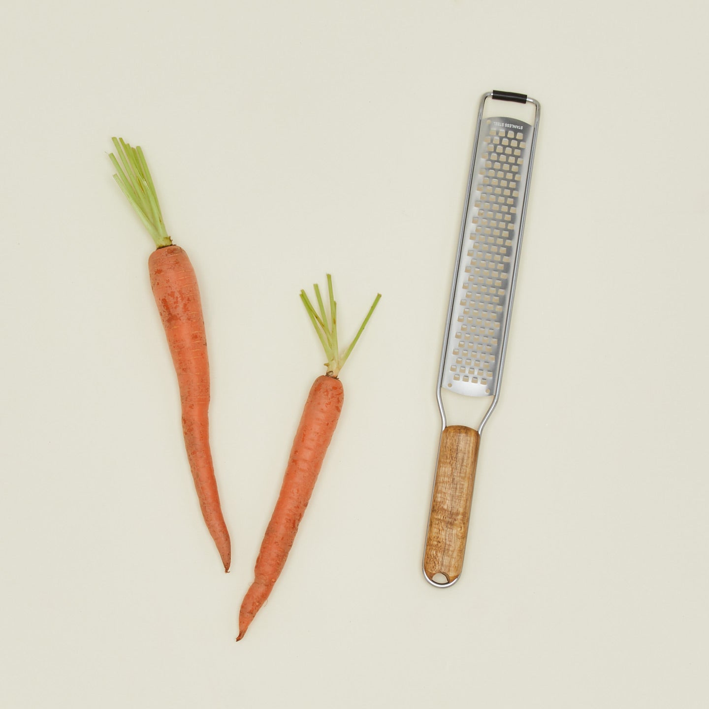 Two carrots and a grater on a beige background