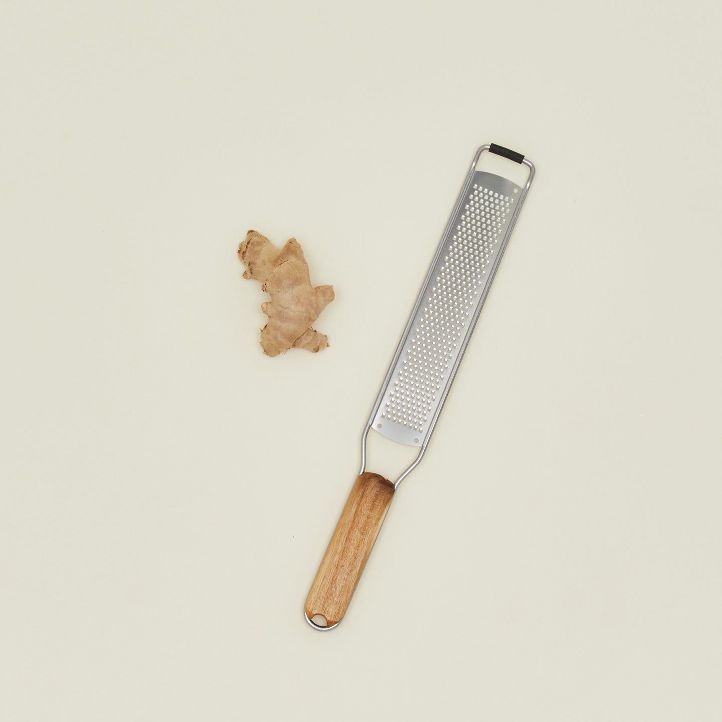 Zester with wooden handle and metal blade next to a piece of ginger on a beige background