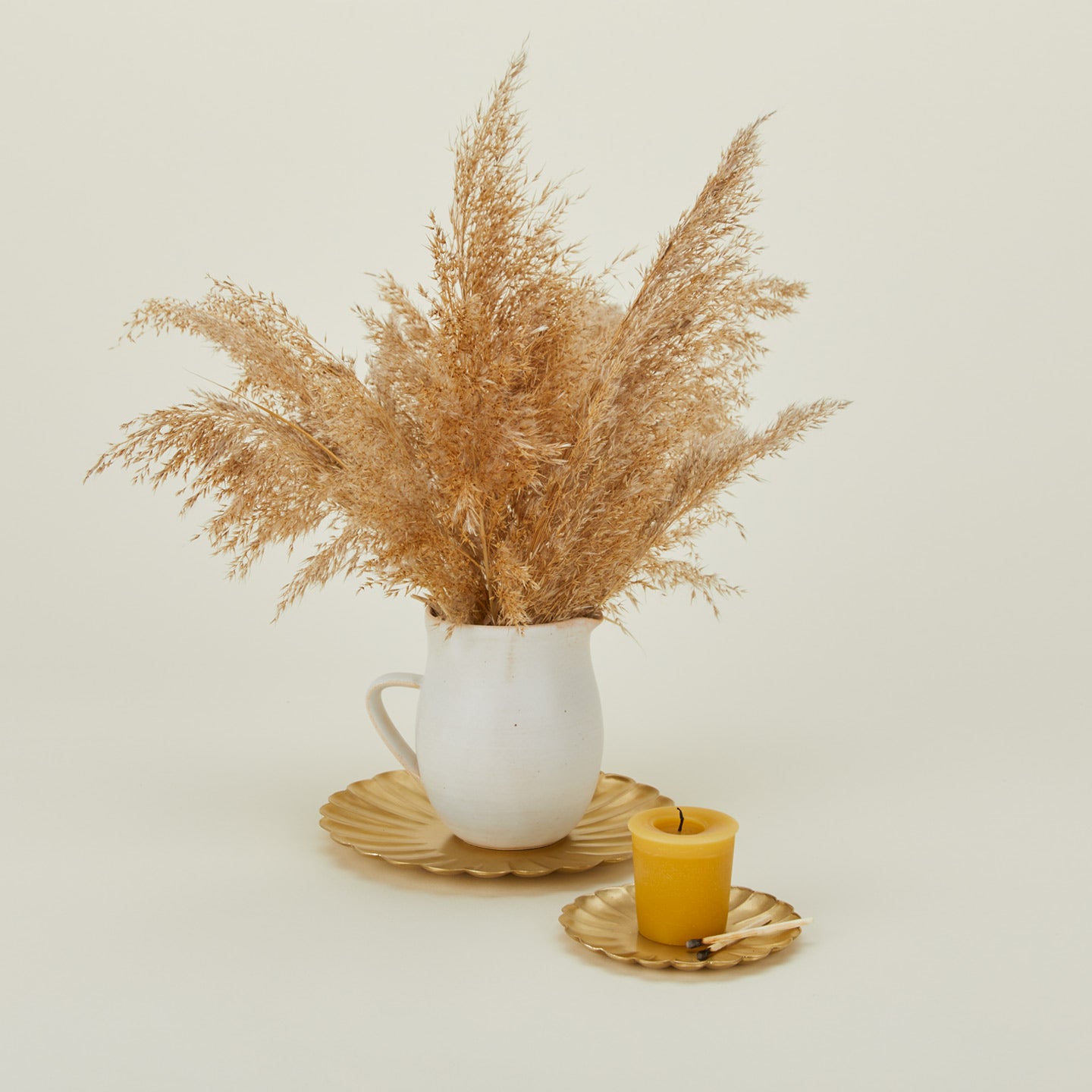 Brass petal plates in large and small with dried florals in a pitcher and a votive candle with matches