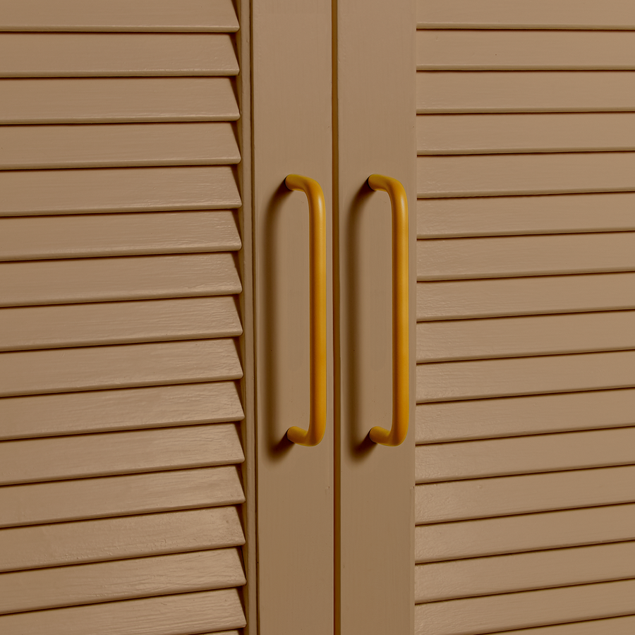 Detail of a brown painted louvered cabinet with mustard colored pull handles.