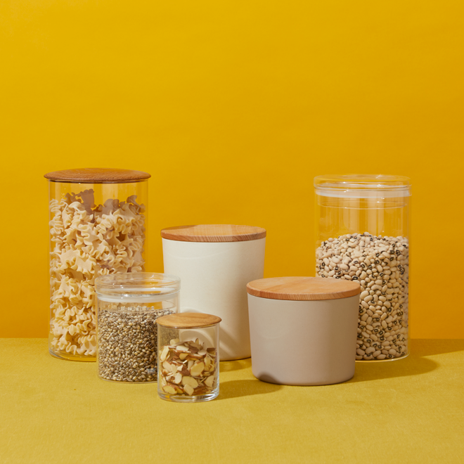 Storage canisters full of dried beans, grains, and pasta arranged against a yellow backdrop.