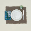 A table setting with bone plates, a green glass, a grey placemat, and an evergreen patterned napkin.