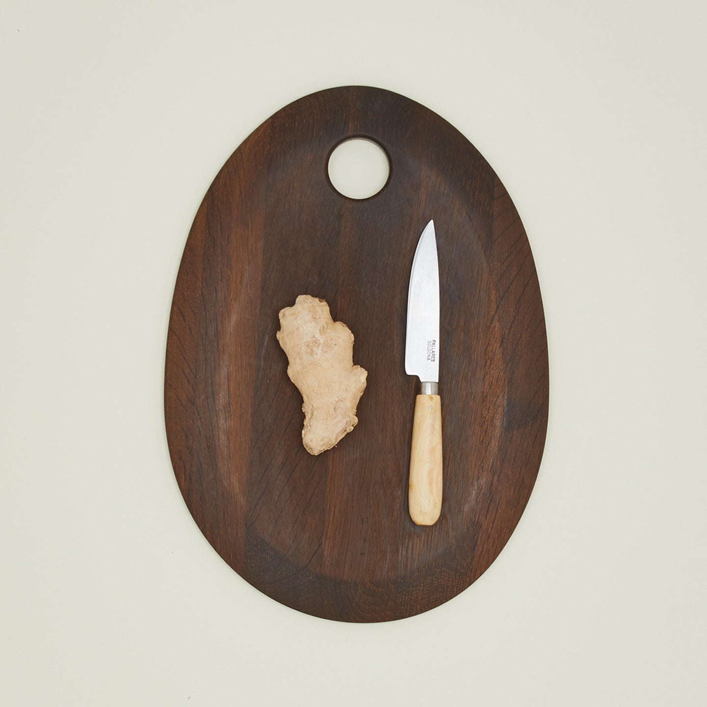 An overhead of a small knife on a walnut cutting board with ginger.