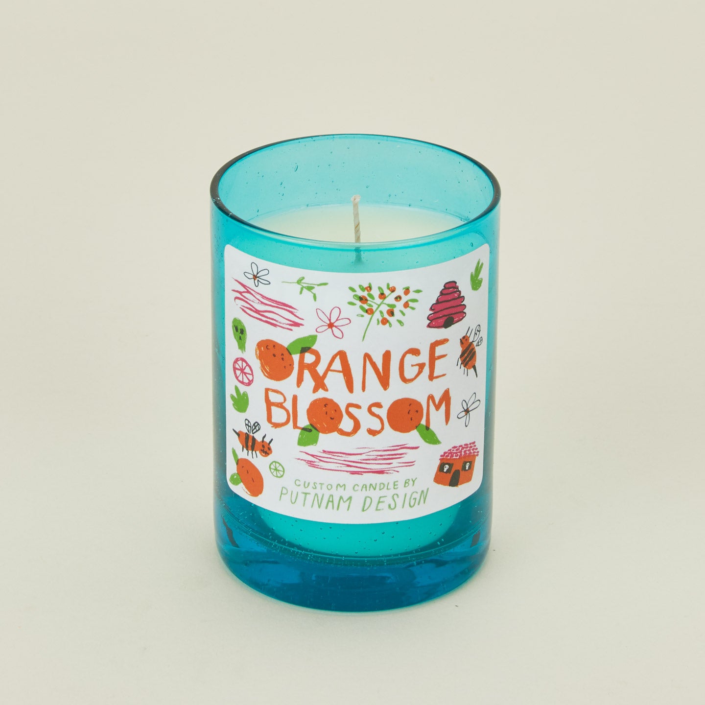 Candle with a blue glass container and colorful label on a beige background