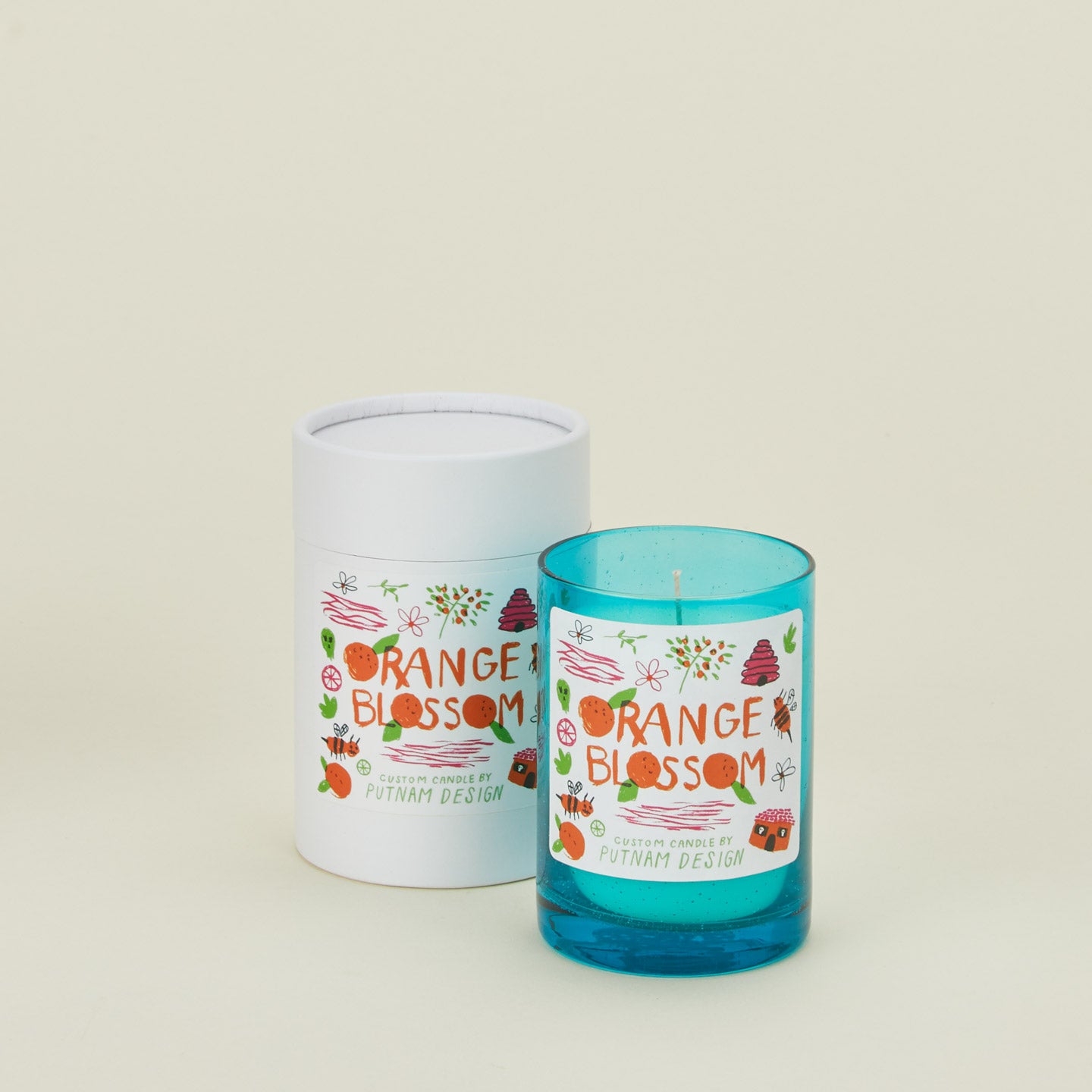 Blue candle with 'Orange Blossom' label and white cylindrical container on a beige background