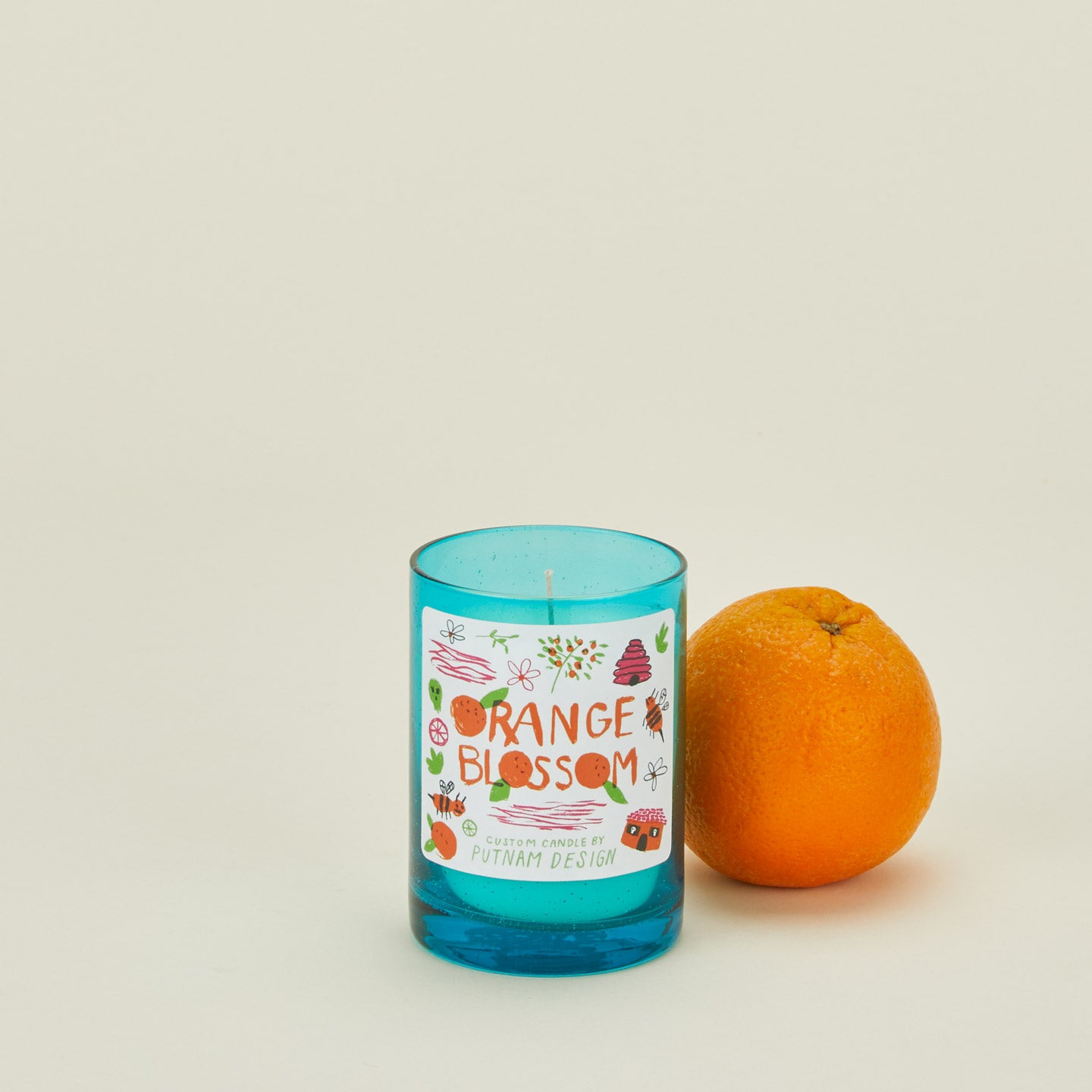 Blue candle labeled 'Orange Blossom' next to an orange on a beige background