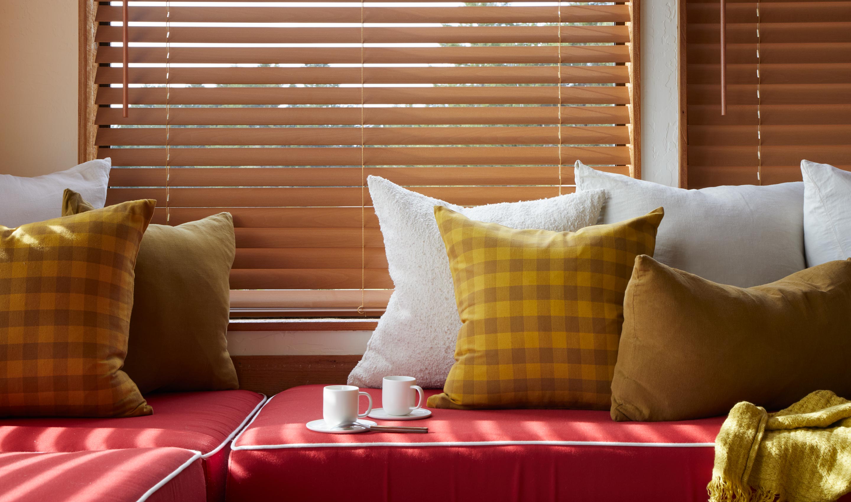Red sofa with yellow and plaid cushions in a room with wooden blinds.