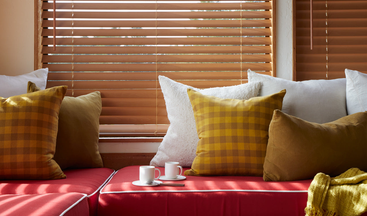 Red sofa with yellow and plaid cushions, wooden blinds in the background
