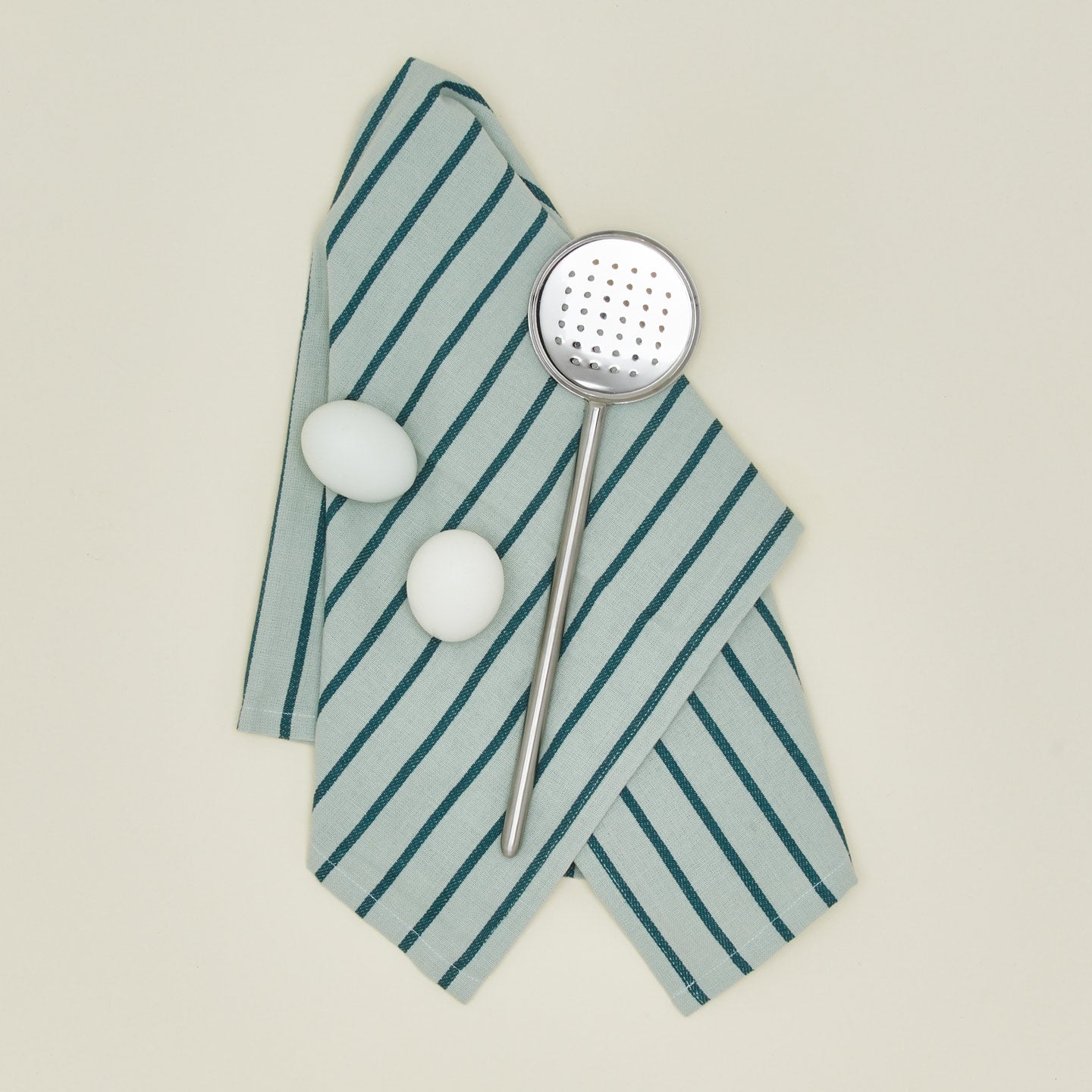Simple metal flat slotted spoon in silver with kitchen towel and eggs
