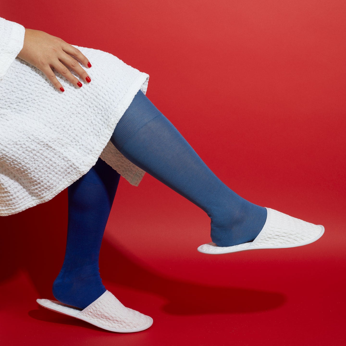 Person wearing blue knee-high socks and white bath slippers and bathrobe on a red background