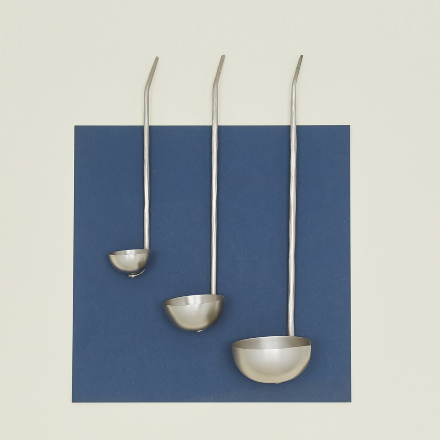 The collective forged pewter ladle set of three on blue paper